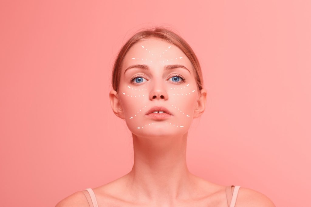 Young beautiful woman close up facial portrait with arrows on her face on pink background.